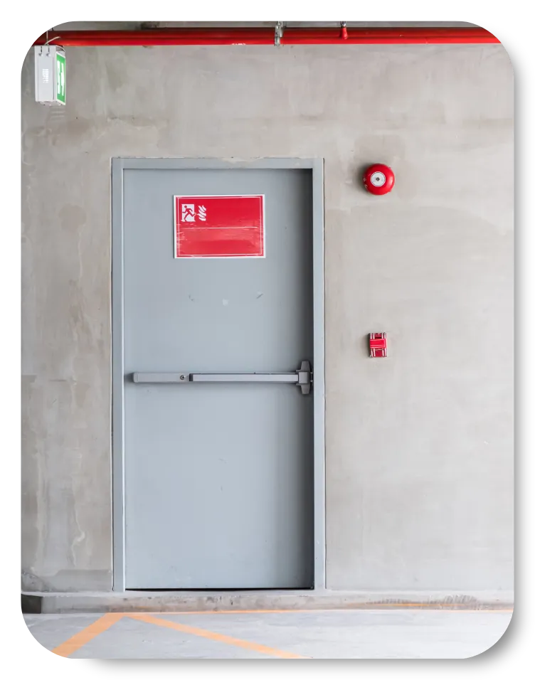 Double red metal doors in a dimly lit hallway with tiled flooring and beige walls.