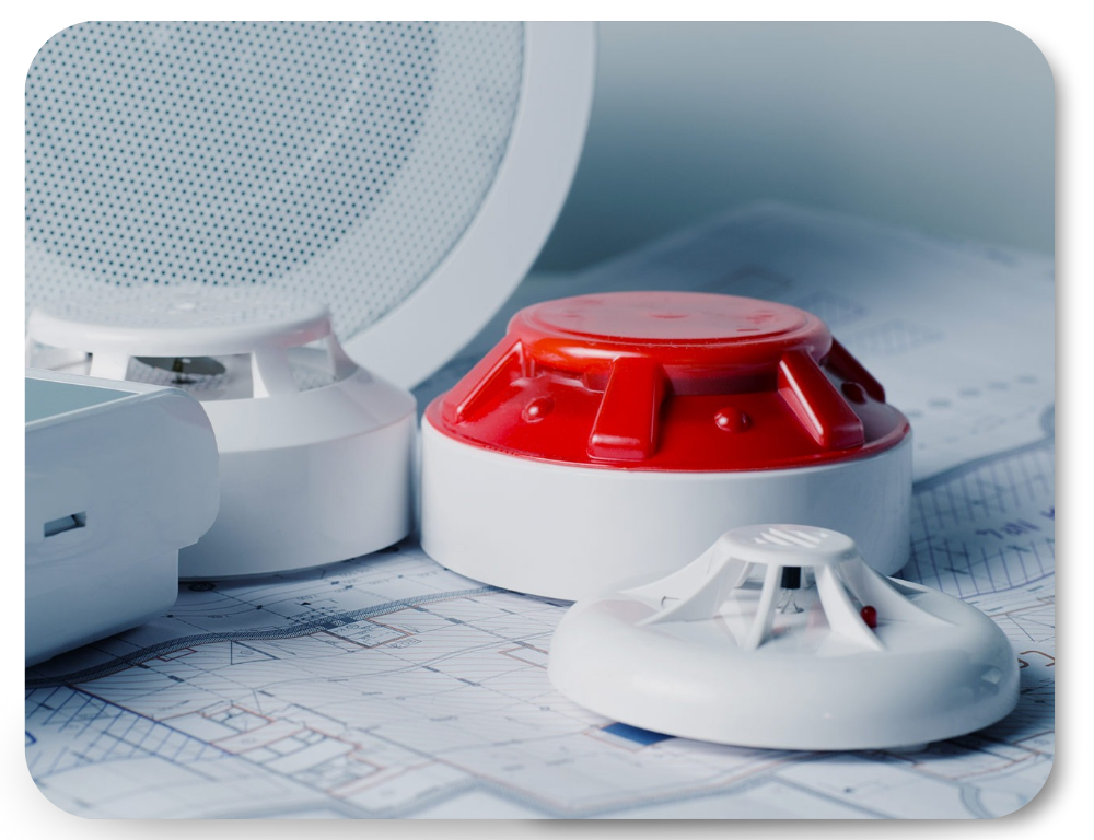 Fire alarm devices including a smoke detector, heat detector, and alarm sounder placed on top of architectural blueprints.