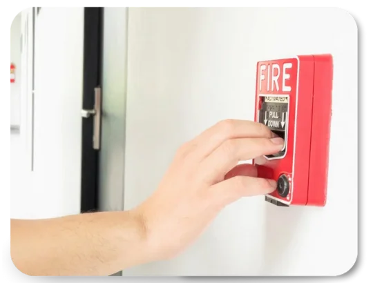 Person pressing red fire alarm manual call point on wall during emergency