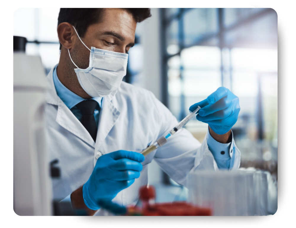 A scientist wearing a mask, gloves, and a lab coat examines a test tube while working in a modern laboratory.